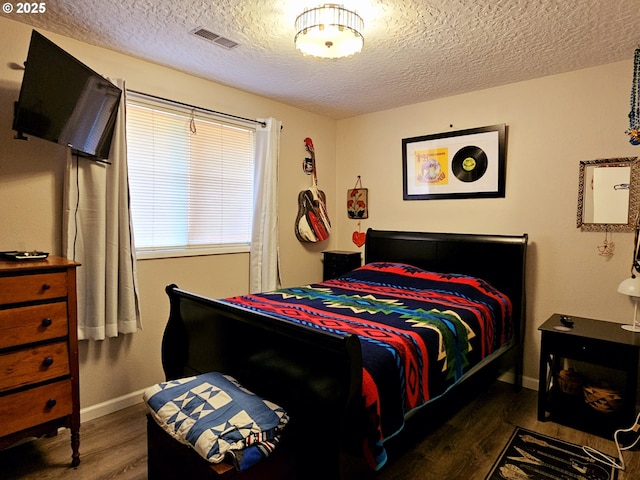 bedroom featuring visible vents, a textured ceiling, baseboards, and wood finished floors