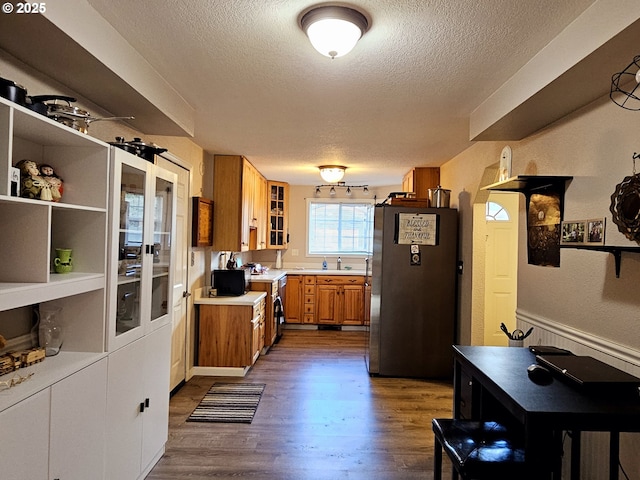 kitchen featuring light countertops, brown cabinetry, dark wood-style flooring, and freestanding refrigerator