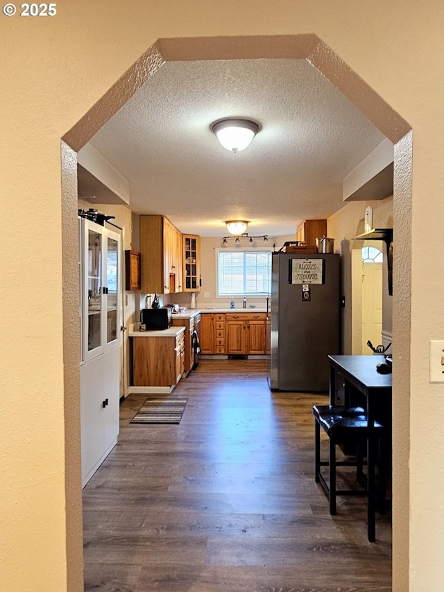 kitchen featuring dark wood-style floors, brown cabinetry, freestanding refrigerator, light countertops, and a textured ceiling