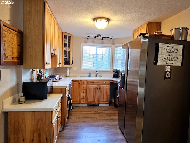 kitchen featuring wood finished floors, stainless steel fridge with ice dispenser, a sink, light countertops, and black microwave