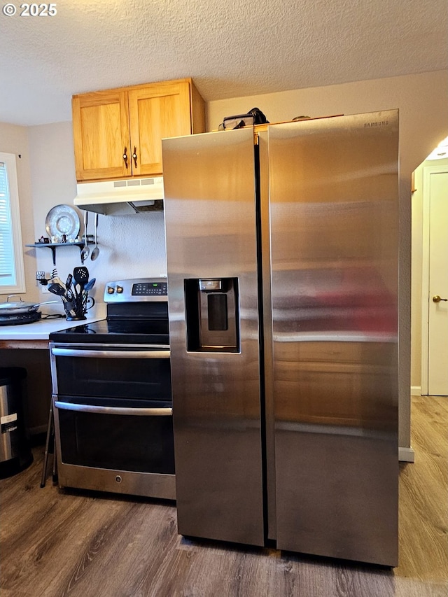 kitchen with under cabinet range hood, a textured ceiling, appliances with stainless steel finishes, and wood finished floors