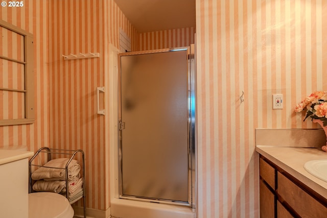 bathroom with toilet, a stall shower, vanity, and wallpapered walls