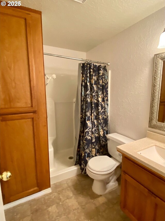 full bath featuring vanity, a textured wall, a shower stall, and toilet