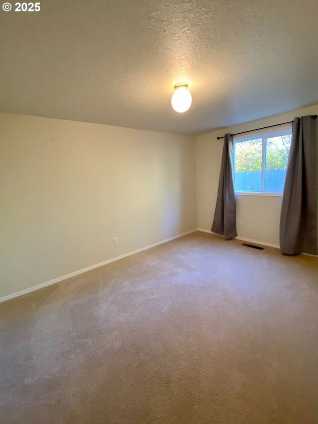 unfurnished room with a textured ceiling, baseboards, light colored carpet, and visible vents