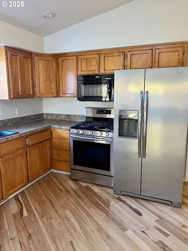 kitchen with brown cabinetry, light wood finished floors, dark countertops, and stainless steel appliances