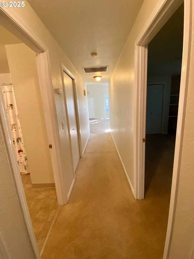 corridor with light colored carpet, baseboards, and visible vents