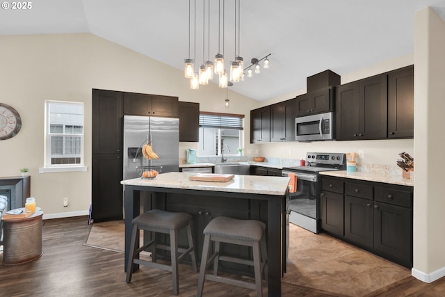 kitchen with vaulted ceiling, a sink, a kitchen bar, appliances with stainless steel finishes, and a kitchen island