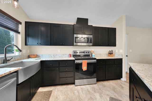 kitchen featuring light stone counters, stainless steel appliances, dark cabinetry, and a sink