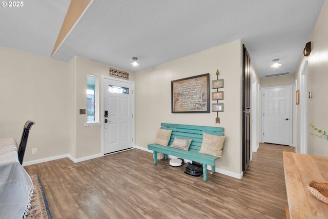 foyer entrance featuring visible vents, baseboards, wood finished floors, and a textured ceiling