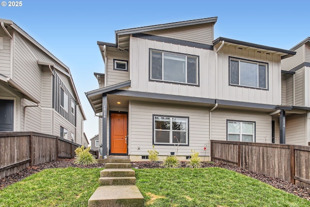 view of front of house with board and batten siding, entry steps, fence, and a front lawn