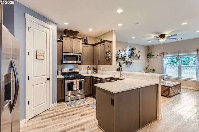 kitchen featuring recessed lighting, a peninsula, a sink, appliances with stainless steel finishes, and light wood-type flooring