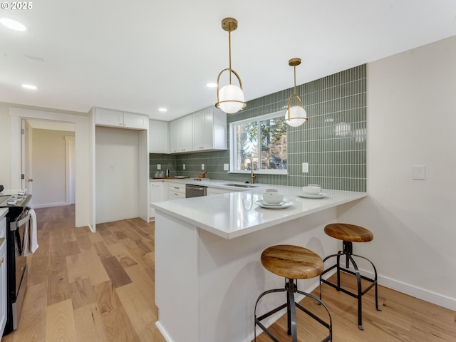 kitchen featuring light wood-style flooring, backsplash, appliances with stainless steel finishes, a sink, and a peninsula