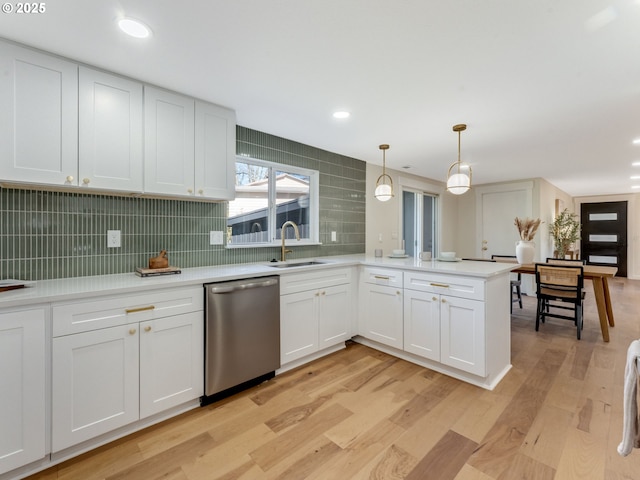 kitchen featuring light wood finished floors, tasteful backsplash, stainless steel dishwasher, a sink, and a peninsula