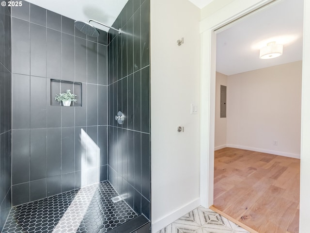 bathroom with electric panel, a tile shower, baseboards, and wood finished floors