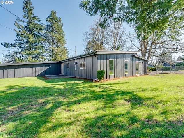 rear view of property with board and batten siding, a lawn, and fence