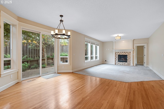 3578 NW Gerritz Ter, Portland, OR 97229 - unfurnished living room with baseboards, a chandelier, light wood finished floors, a tiled fireplace, and a textured ceiling