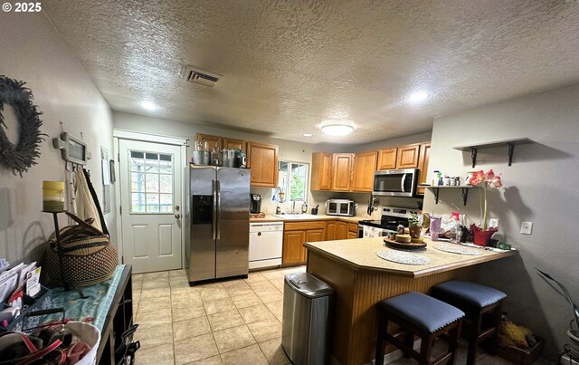 kitchen featuring sink, light tile patterned floors, appliances with stainless steel finishes, a kitchen breakfast bar, and kitchen peninsula