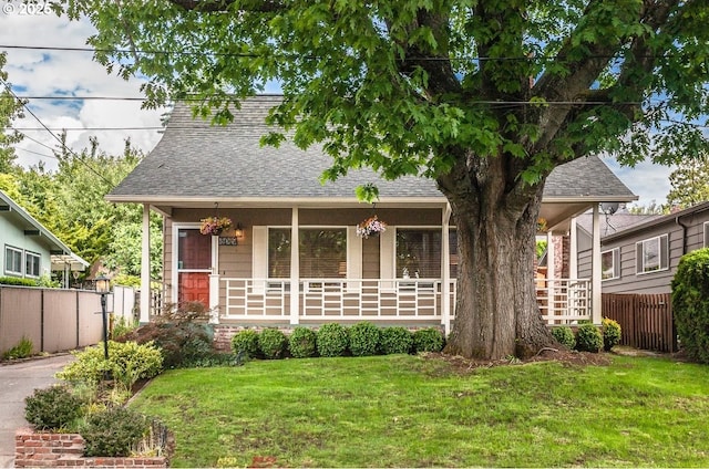 view of front of home with a porch, a shingled roof, a front yard, and fence