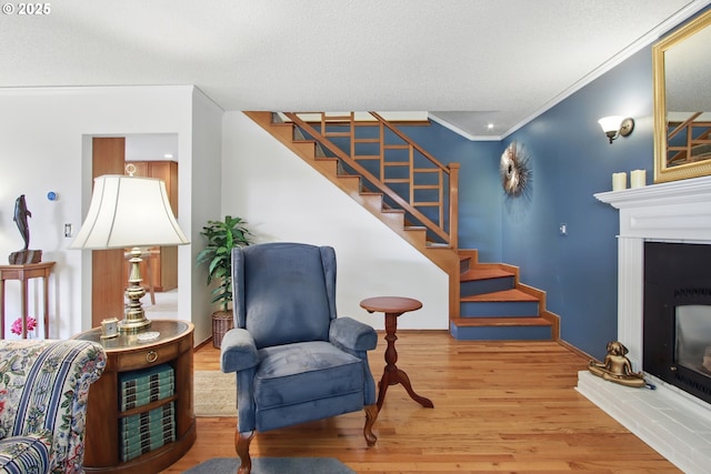 living area with wood finished floors, ornamental molding, a glass covered fireplace, and stairs