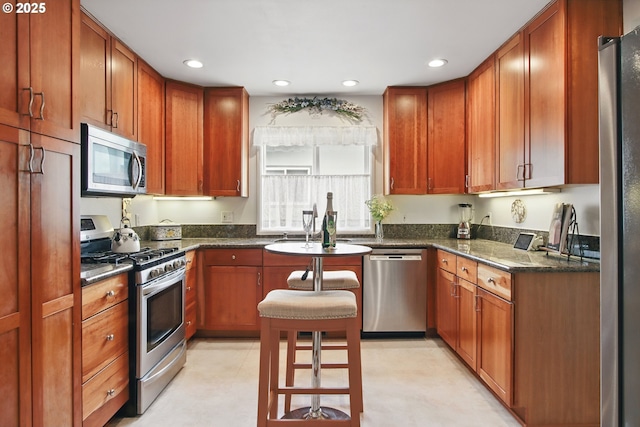 kitchen with brown cabinets, recessed lighting, dark stone countertops, and appliances with stainless steel finishes