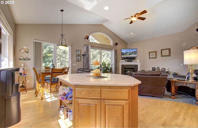 kitchen with light wood-type flooring, ceiling fan, a center island, light stone counters, and decorative light fixtures