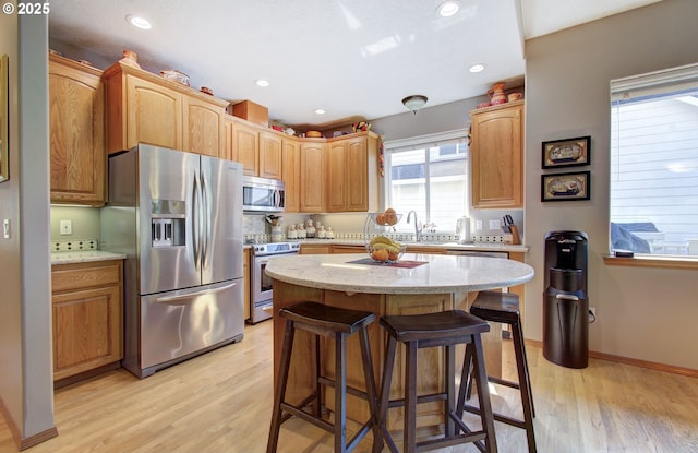 kitchen featuring appliances with stainless steel finishes, light wood-type flooring, a breakfast bar, light stone counters, and recessed lighting