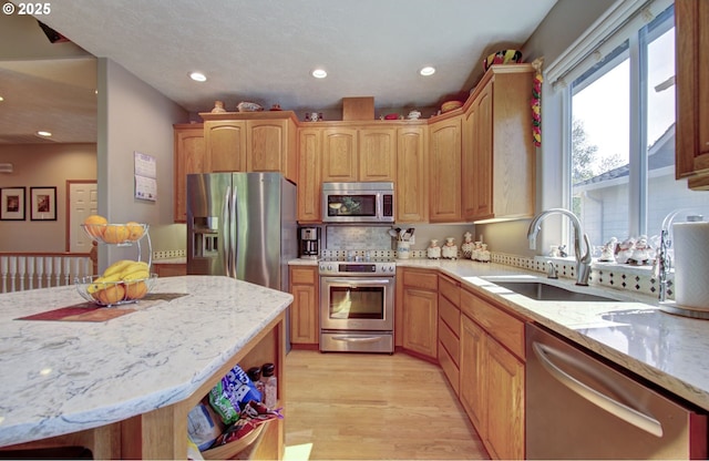 kitchen with appliances with stainless steel finishes, a sink, light wood-style floors, recessed lighting, and light stone countertops