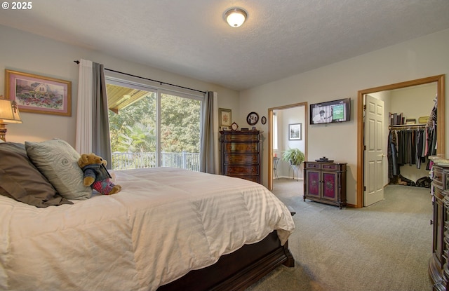 bedroom featuring light colored carpet, a textured ceiling, and a walk in closet