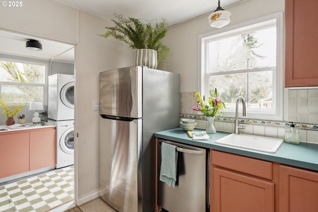 kitchen featuring a sink, a healthy amount of sunlight, stacked washer / drying machine, and stainless steel appliances