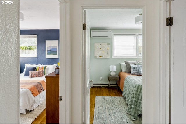 bedroom featuring multiple windows, baseboard heating, an AC wall unit, and wood finished floors