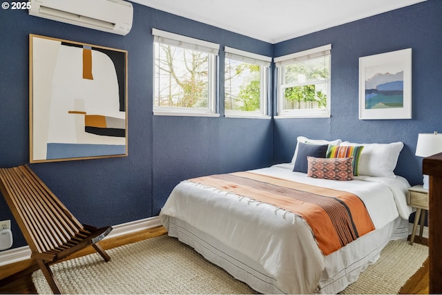 bedroom with a textured wall, baseboards, wood finished floors, and a wall unit AC