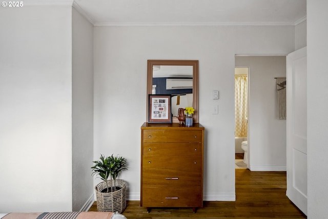 bedroom featuring connected bathroom, crown molding, baseboards, a wall mounted air conditioner, and wood finished floors