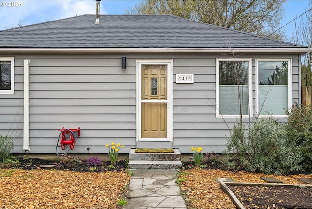 view of exterior entry featuring roof with shingles