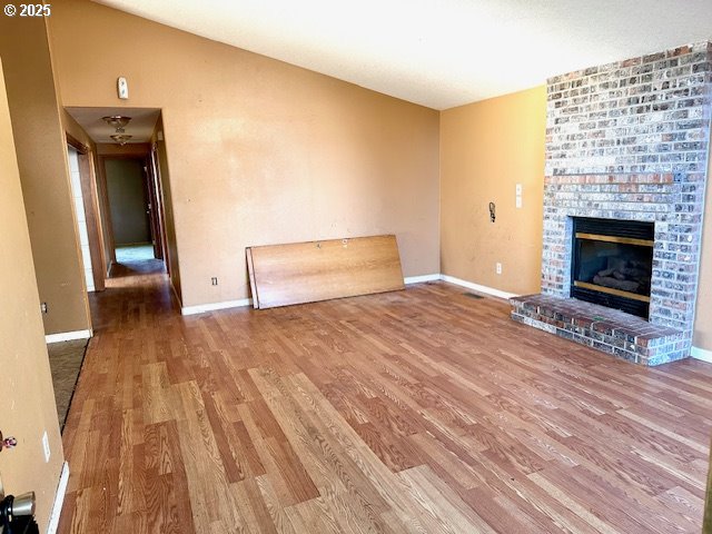 unfurnished living room featuring hardwood / wood-style flooring and a brick fireplace