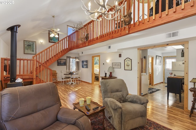 living room with ceiling fan with notable chandelier, a high ceiling, light hardwood / wood-style flooring, and a wood stove