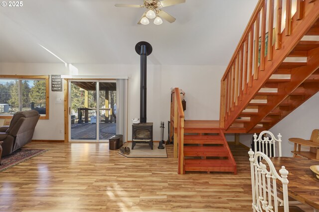 interior space with ceiling fan, wood-type flooring, a healthy amount of sunlight, and a wood stove