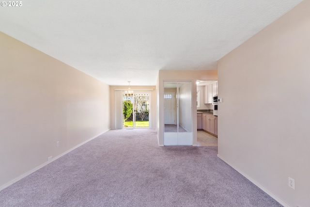 spare room with a textured ceiling, light carpet, and a notable chandelier