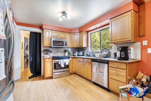 kitchen featuring appliances with stainless steel finishes, a sink, light wood-type flooring, decorative backsplash, and light countertops
