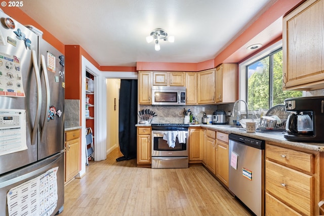 kitchen with stainless steel appliances, light wood-style flooring, tasteful backsplash, light countertops, and a sink