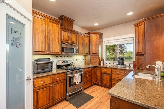 kitchen with light wood-type flooring, brown cabinets, appliances with stainless steel finishes, and a sink