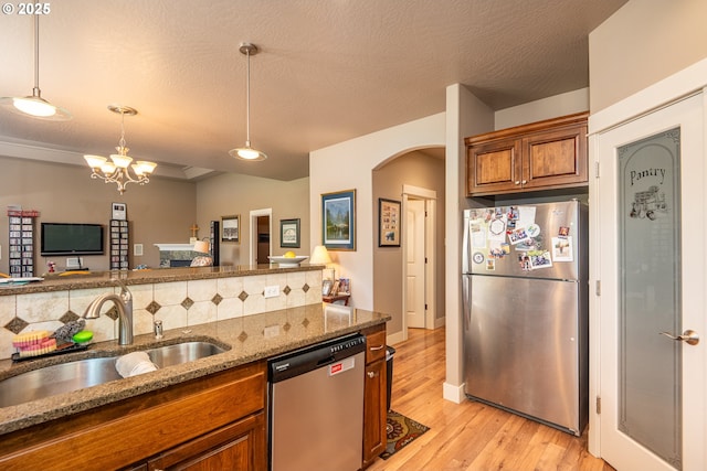 kitchen with a sink, brown cabinetry, stainless steel appliances, arched walkways, and light stone countertops