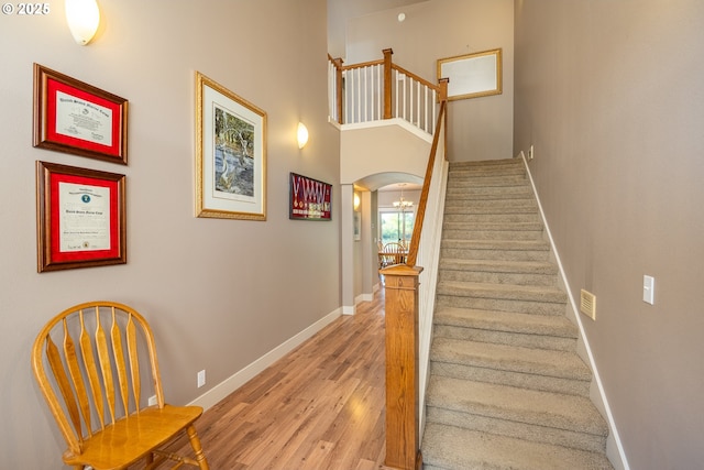 stairs with a towering ceiling, arched walkways, baseboards, and wood finished floors