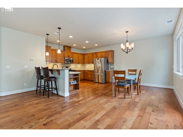 kitchen featuring visible vents, brown cabinetry, a peninsula, light wood-style floors, and stainless steel appliances