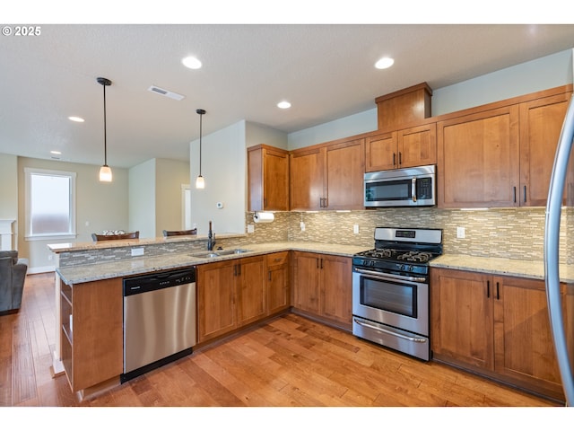 kitchen featuring brown cabinetry, a sink, light wood-style flooring, and appliances with stainless steel finishes
