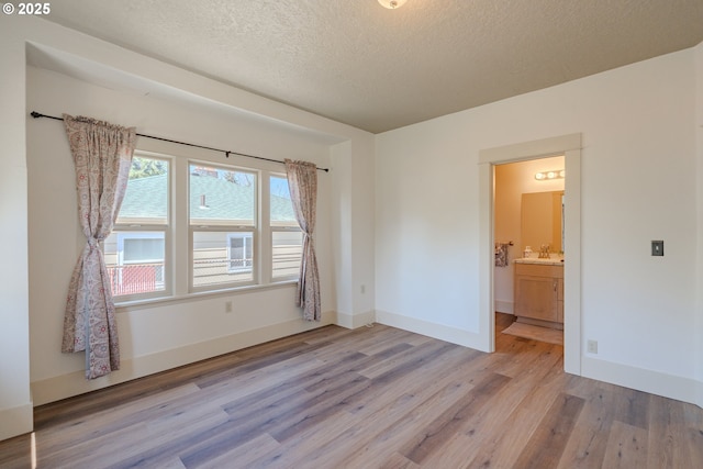 7906 SE Woodstock Blvd, Portland, OR 97206 - empty room with light wood-type flooring, a textured ceiling, a sink, and baseboards