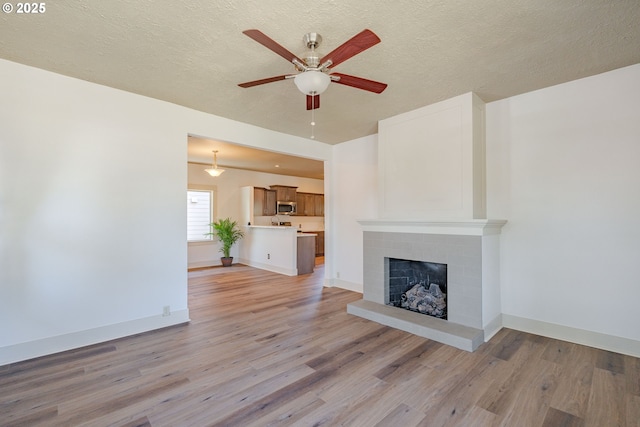 7906 SE Woodstock Blvd, Portland, OR 97206 - unfurnished living room featuring a ceiling fan, light wood-style floors, a brick fireplace, a textured ceiling, and baseboards