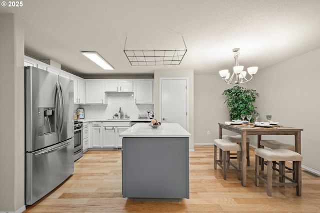 kitchen with sink, decorative light fixtures, appliances with stainless steel finishes, a kitchen island, and white cabinets