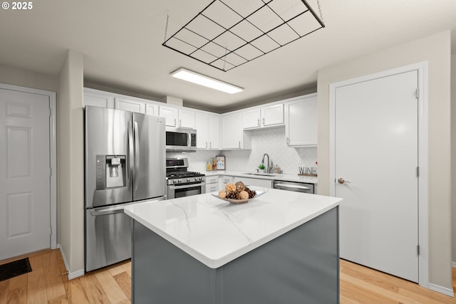 kitchen with a kitchen island, white cabinetry, sink, stainless steel appliances, and light stone countertops