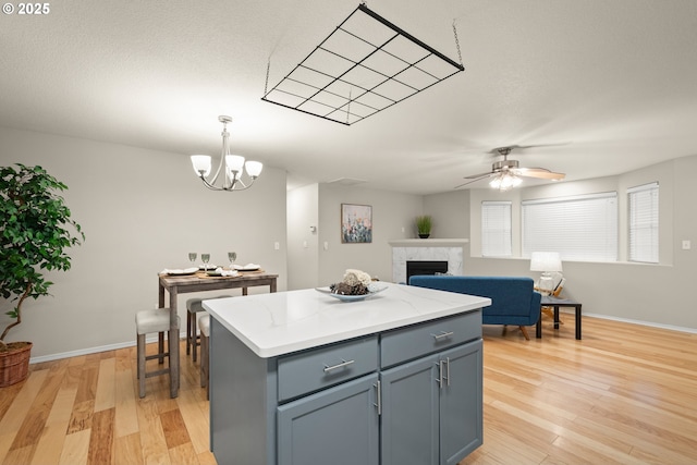 kitchen with pendant lighting, a tile fireplace, a kitchen island, ceiling fan with notable chandelier, and light wood-type flooring