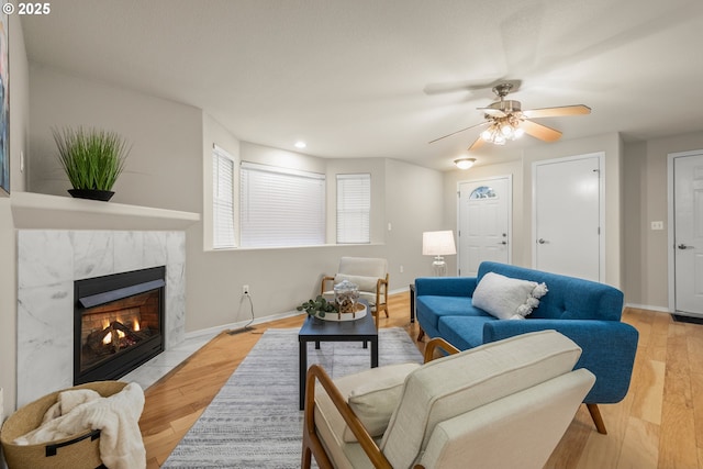 living room with light hardwood / wood-style floors, a premium fireplace, and ceiling fan